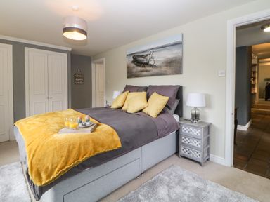 A bedroom with a bed with yellow pillows and blanket a bedside table with a lamp and a painting above the bed at Lower Culvermead in Chaddlehanger near Tavistock