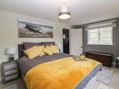 A bedroom with a bed featuring yellow pillows and blanket a wooden chest under a window and a door on the side at Lower Culvermead in Chaddlehanger near Tavistock