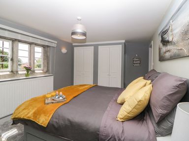 A bedroom with a bed having yellow pillows and a yellow throw blanket next to a window with flowers on the sill at Lower Culvermead in Chaddlehanger near Tavistock