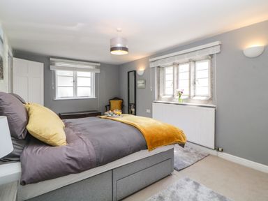 A bedroom with a bed a yellow throw and pillows a chair a window and a radiator at Lower Culvermead in Chaddlehanger near Tavistock