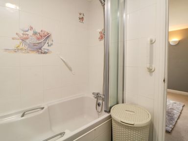A bathroom with a bathtub featuring animal-themed tile decorations and a laundry basket at Lower Culvermead in Chaddlehanger near Tavistock
