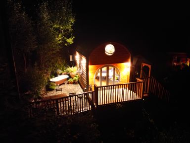 A wooden tiny house with a round window and a deck surrounded by plants and outdoor furniture at The Kites Nest in Pont-rhyd-y-groes near Pontrhydfendigaid Snowdonia