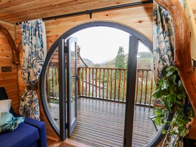 A wooden room with a circular glass door opening onto a balcony with wooden railings at The Kites Nest in Pont-rhyd-y-groes near Pontrhydfendigaid Snowdonia