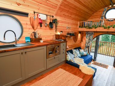 A small kitchen with sink microwave and hanging utensils next to a blue sofa with cushions and a balcony at The Kites Nest in Pont-rhyd-y-groes near Pontrhydfendigaid Snowdonia