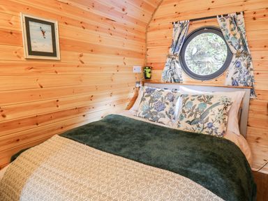 A bedroom with a bed with floral pillows and a circular window with floral curtains at The Kites Nest in Pont-rhyd-y-groes near Pontrhydfendigaid Snowdonia