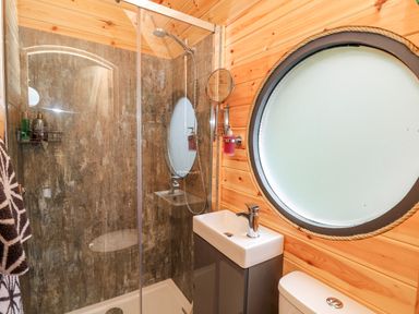 A bathroom with a shower enclosure, sink, toilet, and a round frosted window at The Kites Nest in Pont-rhyd-y-groes near Pontrhydfendigaid Snowdonia