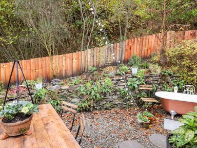 An outdoor patio area with wooden table and chairs a clawfoot bathtub string lights and plants at The Kites Nest in Pont-rhyd-y-groes near Pontrhydfendigaid Snowdonia