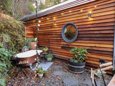 An outdoor area with a freestanding bathtub wooden chairs plants and string lights by a wooden building at The Kites Nest in Pont-rhyd-y-groes near Pontrhydfendigaid Snowdonia