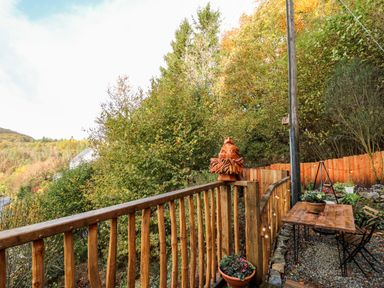 A wooden deck with a table and chairs surrounded by trees and a wooden fence at The Kites Nest in Pont-rhyd-y-groes near Pontrhydfendigaid Snowdonia