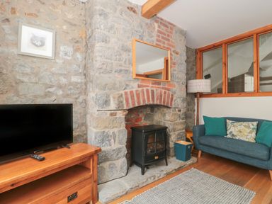 A living room with a stone fireplace a wood stove a blue sofa and a television on a wooden stand at Teal House in Lyme Regis