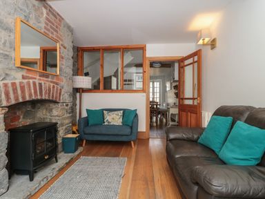 A living room with a stone fireplace a black stove two sofas with cushions and a wooden floor at Teal House in Lyme Regis