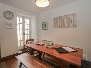 A dining area with a wooden table bench and chair next to white French doors at Teal House Lyme Regis