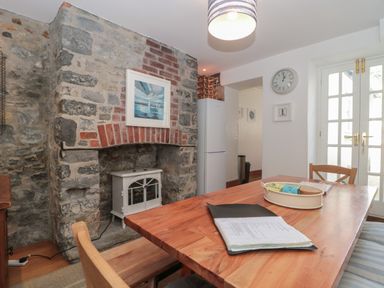 A dining room with a wooden table and chairs near a stone fireplace and white fridge at Teal House in Lyme Regis