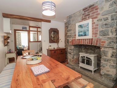 A dining area with a wooden table, chairs, a stone fireplace, a framed painting above the fireplace, and a wooden cabinet at Teal House in Lyme Regis