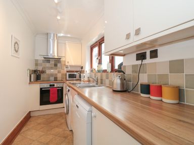 A kitchen with wooden countertops, white cabinets, stainless steel oven and kettle, tiled backsplash at Teal House Lyme Regis
