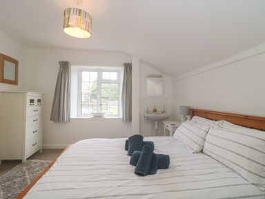 A bedroom with a bed with striped bedding a window with curtains a chest of drawers and a washbasin at Teal House Lyme Regis