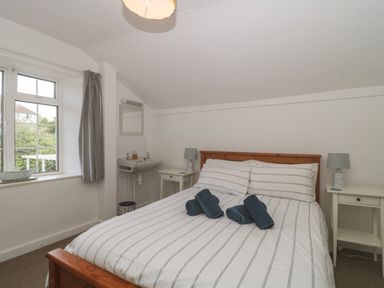 A bedroom with a wooden bed with striped bedding a window with a curtain two bedside tables with lamps and a sink with a mirror at Teal House in Lyme Regis