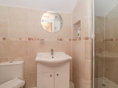 A small bathroom with a white sink cabinet a round mirror a toilet and a glass shower at Teal House in Lyme Regis