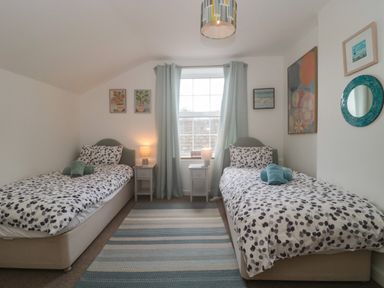 A bedroom with two single beds a window with curtains and a rug on the floor at Teal House in Lyme Regis
