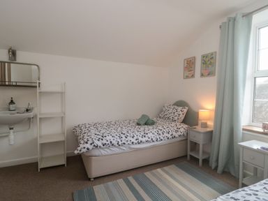 A bedroom with a single bed bedside table lamp and window with curtains at Teal House in Lyme Regis