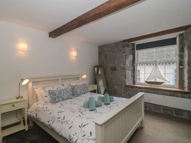 A bedroom with a bed between two nightstands and a window with a model sailboat on the sill at Teal House in Lyme Regis