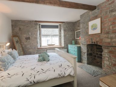 A bedroom with a bed with patterned bedding and rolled towels a wooden dresser a window with a model sailboat and a stone fireplace at Teal House Lyme Regis