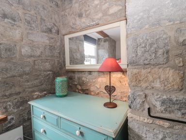 A turquoise chest of drawers with a green vase and red lampshade on a stone wall at Teal House in Lyme Regis