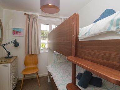 A bedroom with bunk beds a wooden chair a small chest of drawers with a desk lamp and a window with curtains at Teal House in Lyme Regis