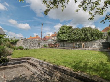 A backyard with a grass lawn wooden steps and outdoor dining tables with chairs at Teal House in Lyme Regis
