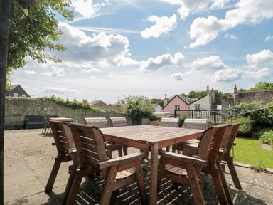 An outdoor patio area with a wooden dining table and chairs next to a stone wall and garden at Teal House Lyme Regis
