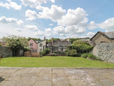 A garden with grass and plants bordered by stone walls and houses in the background at Teal House in Lyme Regis