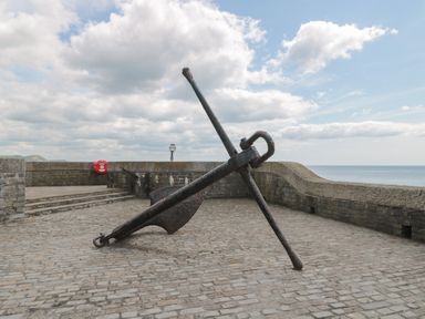 A large anchor on a paved area near a stone wall with the sea and sky in the background at Teal House in Lyme Regis