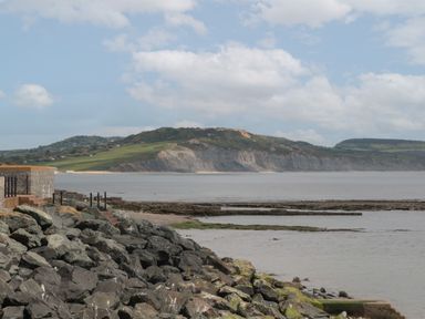 A rocky shoreline with a stone wall and steps leading to the water and cliffs in the background at Teal House in Lyme Regis