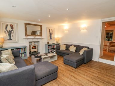 A living room with two gray sofas a coffee table a wood stove a large mirror and lobster artwork at Tan y Craig in Solva