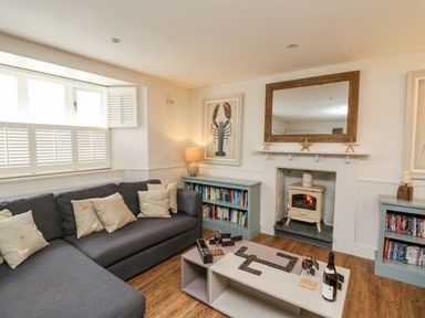 A living room with a sofa a coffee table with dominoes and wine a fireplace and bookshelves at Tan y Craig in Solva