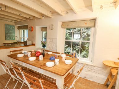 A dining room with a wooden table and chairs set with bowls mugs and teapots next to windows at Tan y Craig in Solva