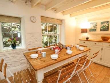 A dining room with a wooden table and chairs set with bowls mugs and teapots at Tan y Craig in Solva