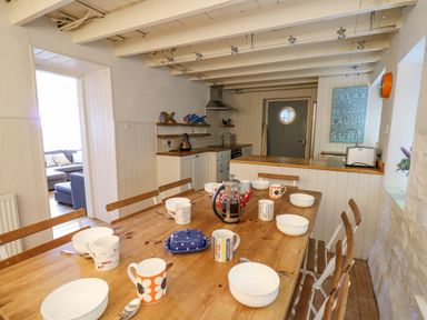 A kitchen with a wooden dining table set with bowls mugs and a coffee press at Tan y Craig in Solva