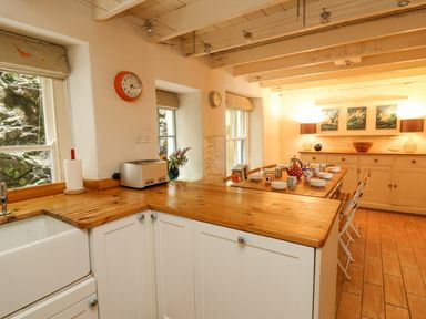 A kitchen with wooden countertops a dining table set with cups and bowls and a sideboard with lamps and paintings at Tan y Craig in Solva