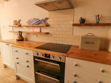A kitchen countertop with a stove drawer cabinets a bread box kettle and wooden fish decorations on shelves at Tan y Craig in Solva
