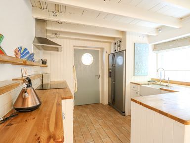 A kitchen with wooden countertops a silver kettle a stainless steel fridge a grey door with a round window and a window above the sink at Tan y Craig in Solva