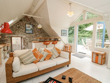 A living room with a woven sofa with cushions a coffee table a stone wall and large glass doors opening to a patio at Tan y Craig in Solva