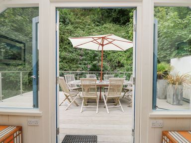 A patio with a wooden table and chairs under a large umbrella surrounded by greenery at Tan y Craig in Solva