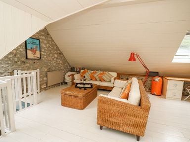 A sitting area with wicker sofas and a coffee table under a sloped ceiling at Tan y Craig in Solva