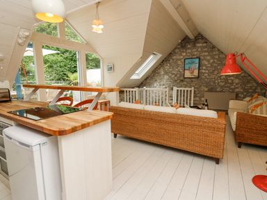 A small living area with wicker sofas a kitchen counter with a wooden top and glass doors leading outside at Tan y Craig in Solva