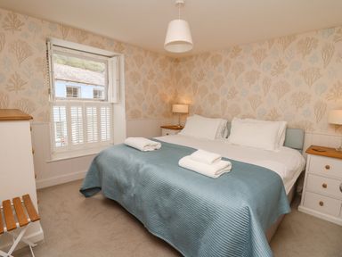 A bedroom with a double bed covered with a blue quilt and white pillows two bedside tables with lamps and a window with shutters at Tan y Craig in Solva