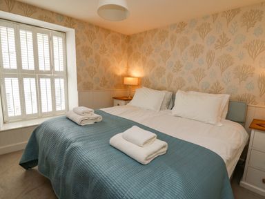 A bedroom with a double bed white pillows blue bedspread bedside tables lamps and shuttered window at Tan y Craig in Solva