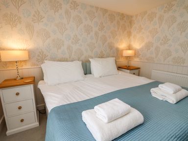 A bedroom with a double bed with white pillows and folded towels on a blue quilt with two bedside tables and lamps at Tan y Craig in Solva