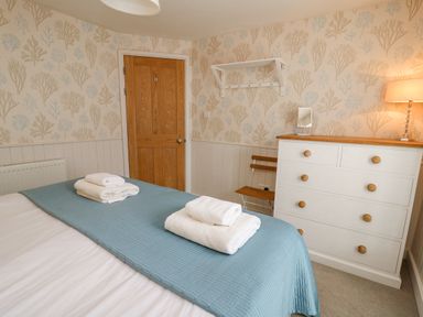 A bedroom with a bed with folded towels a wooden door a white dresser a small chair and patterned wallpaper at Tan y Craig Solva