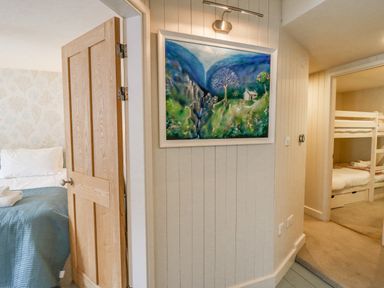 A hallway with a painting on the wall and two doorways leading to a bedroom with a bed and a room with bunk beds at Tan y Craig in Solva